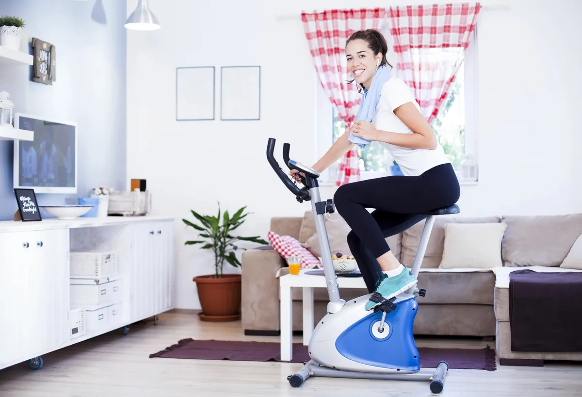 Frau trainiert auf einem Heimtrainer im Wohnzimmer