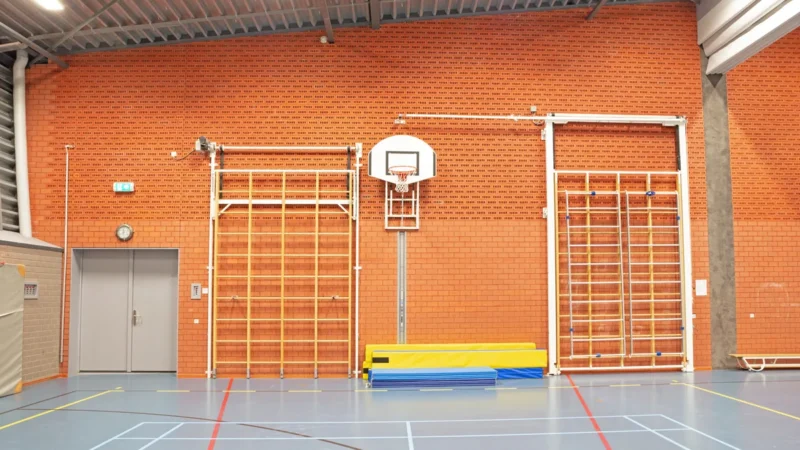 Schulsporthalle mit Sprossenwänden, Basketballkorb und Turnmatten